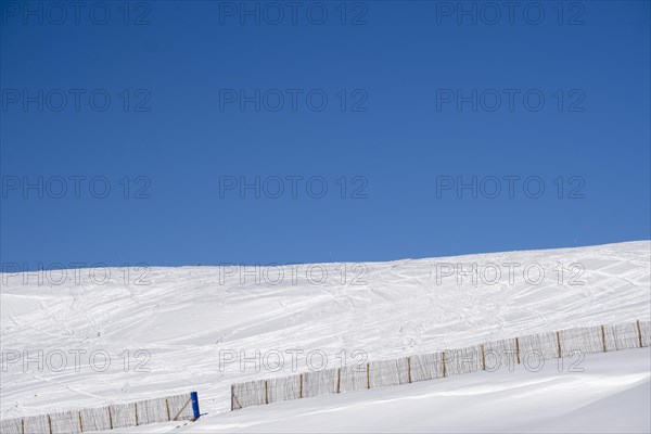Minimalist landscape on a snowy mountain with a fence with blue sky