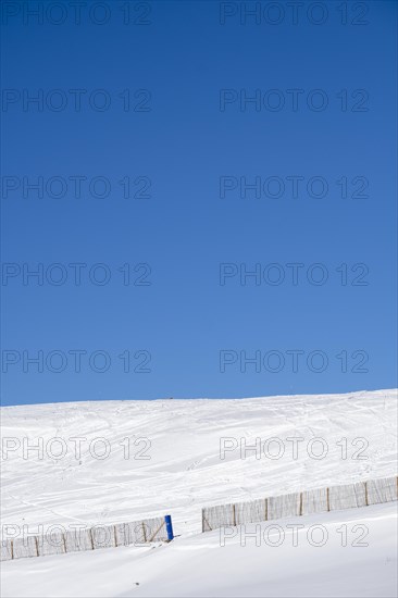 Minimalist landscape on a snowy mountain with a fence with blue sky