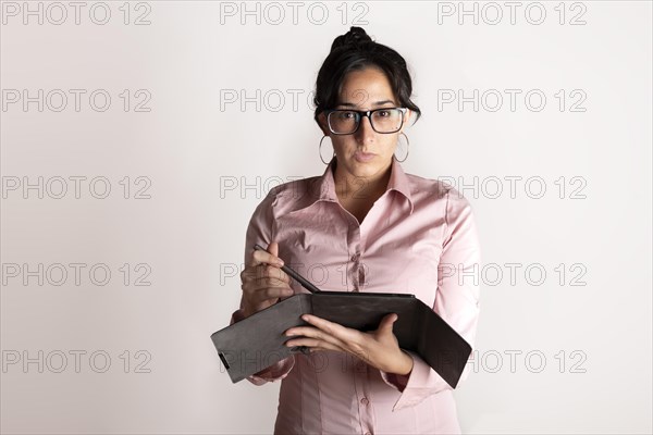 Brunette latin business woman wearing a pink shirt with a tablet in her hands on white studio background looking seriously at the camera
