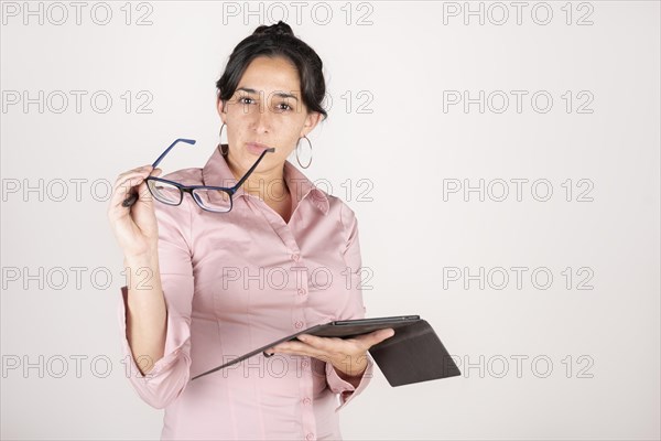 Brunette latin business woman wearing a pink shirt with a tablet in her hands on white studio background looking seriously at the camera