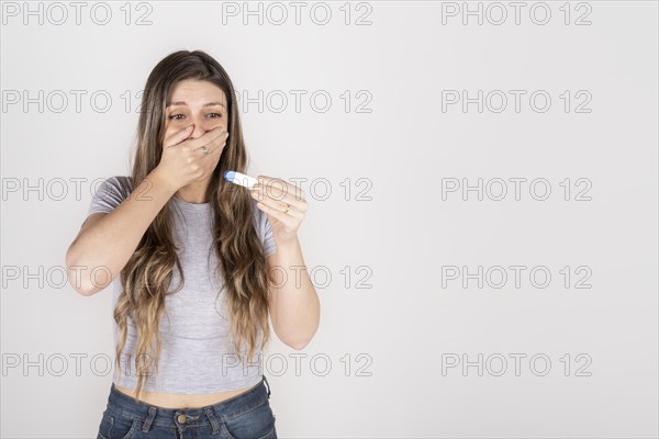 Portrait of a young blond woman holding pregnancy test feeling shocked