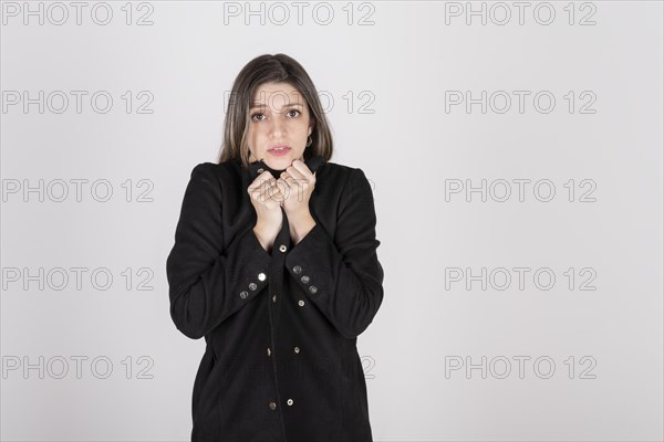 Studio portrait of young blonde woman wearing a black coat with expression of cold and disgust