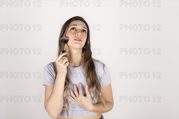 Blonde woman passing makeup brush over her face on white studio background