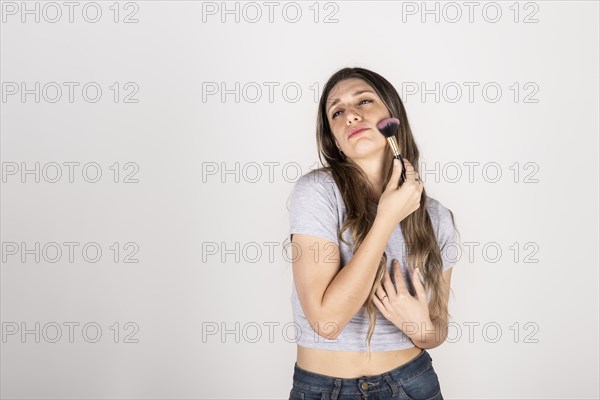 Blonde woman passing makeup brush over her face on white studio background