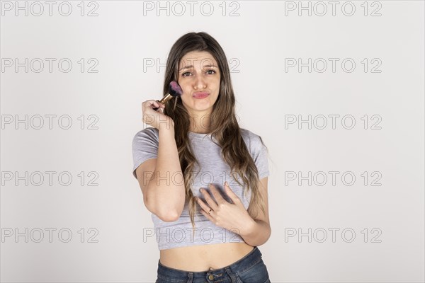 Blonde woman passing makeup brush over her face on white studio background
