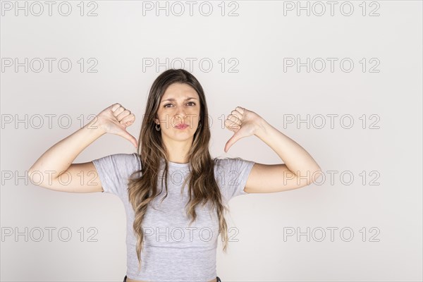 Blonde woman looking at camera with two thumbs down on white studio background. Concept of disapproval