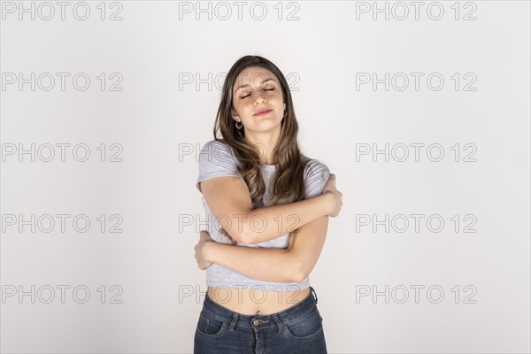 Portrait of a blonde young woman hugging herself on white studio background