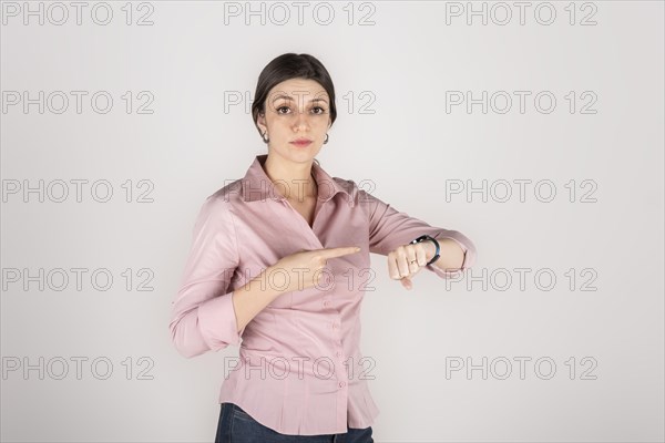 Young beautiful latin american blond business woman standing over white background in hurry pointing to watch time