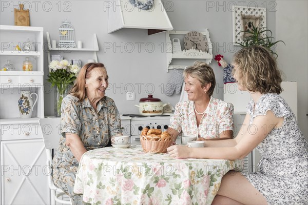 Mother grand daughter granny sitting kitchen smiling