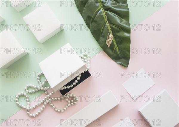 Overhead view pearl necklace golden earrings with white boxes paper background