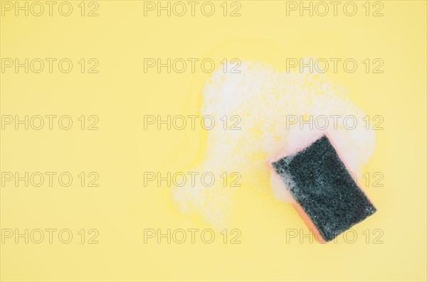 Overhead view sponge with soap sud yellow background