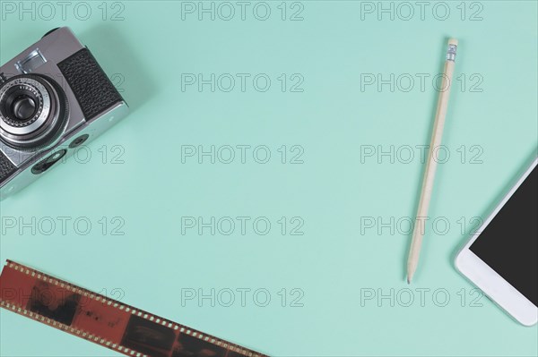 Pencil mobile phone camera old film strip against turquoise background
