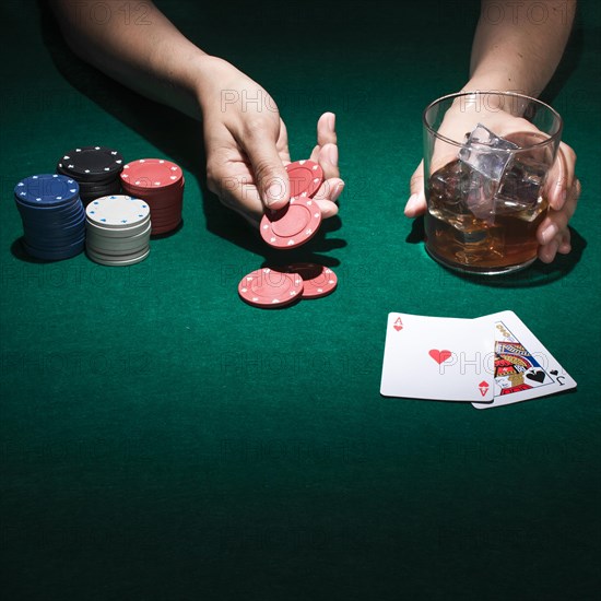 Person holding glass whiskey while playing poker card