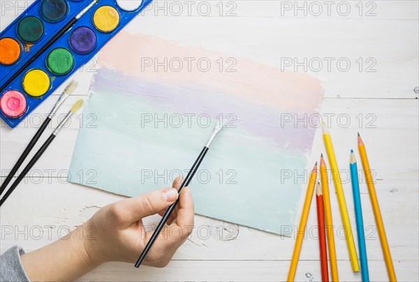 Person s hand painting paper with paint brush watercolor desk