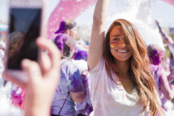 Person taking selfie her smiling female friend mobile phone during holi