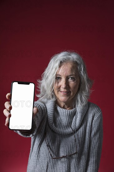 Portrait senior woman showing mobile phone with blank white screen display