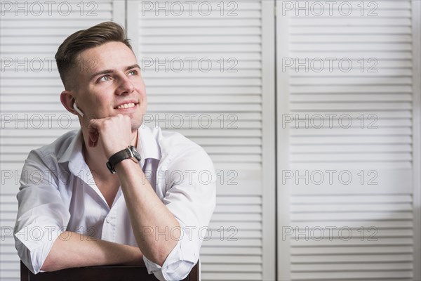 Portrait smiling young man with wireless earphone his ear looking away