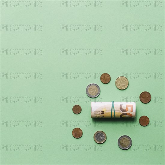 Rolled up euro bank note with coins green backdrop