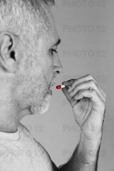 Senior man taking red white capsule