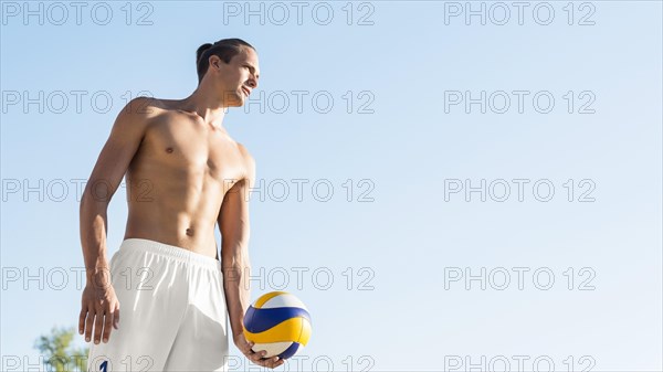 Shirtless male volleyball player preparing serve ball with copy space