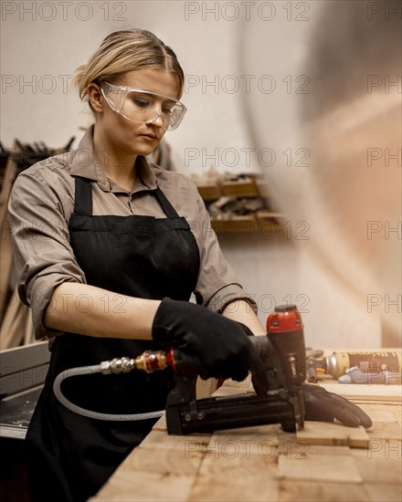 Side view female carpenter with pneumatic stapler studio