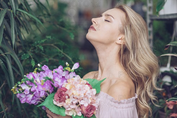 Side view relaxed young woman standing garden holding colorful flower bouquet