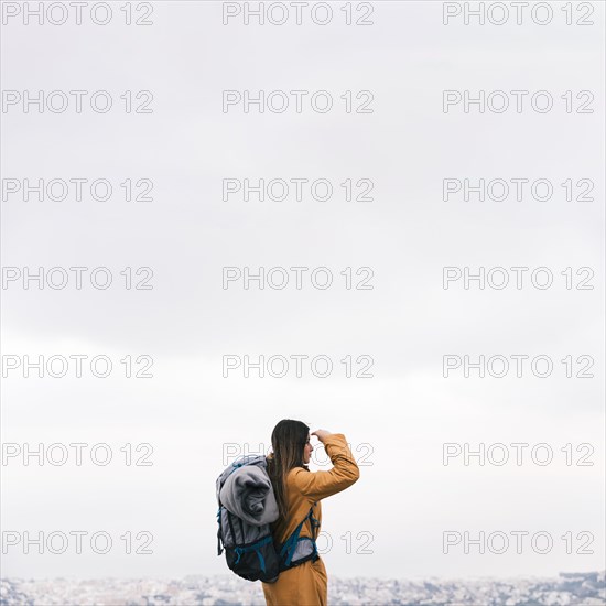 Side view young female hiker with her backpack overlooking cityscape against sky