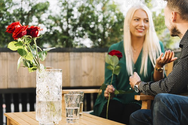 Smiling beautiful young woman holding red rose talking his boyfriend