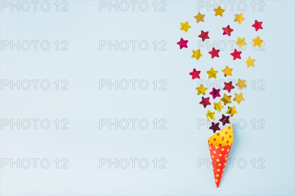 Star shape confetti coming out from paper cone with polka dot blue background