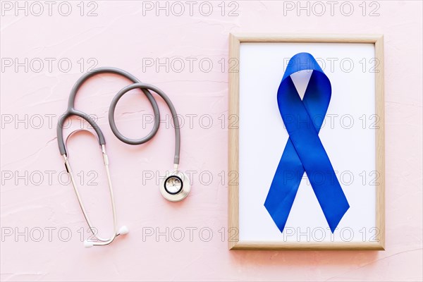 Stethoscope near wooden frame with blue awareness ribbon