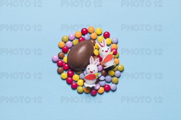 Two white bunnies chocolate easter egg colorful gem candies against blue background