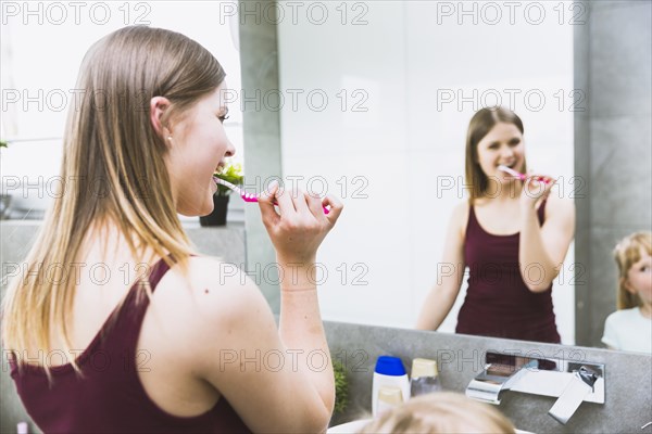 Woman brushing teeth near mirror