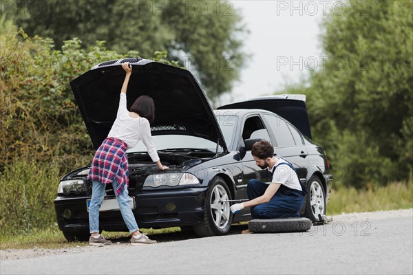 Woman checking engine man swapping tire