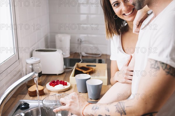 Woman looking man washing dishes