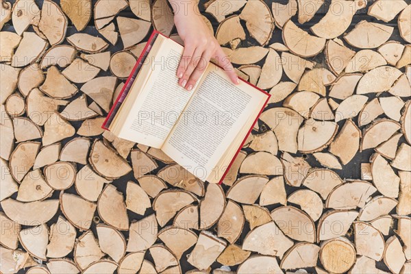 Woman s hand holding book against firewood stack wall