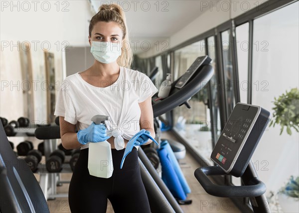 Woman with gloves cleaning gym equipment with medical mask during pandemic