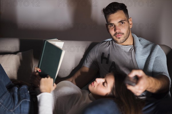 Young man with tv remote woman with book sofa