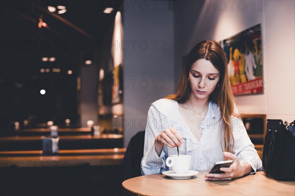 Young woman with smartphone mixing beverage