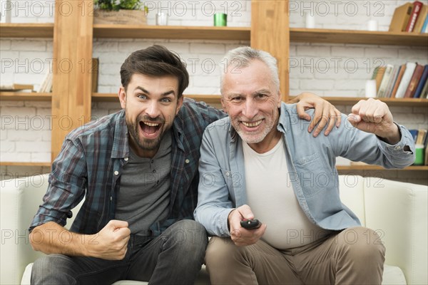 Aged happy man with remote control young crying guy watching tv sofa