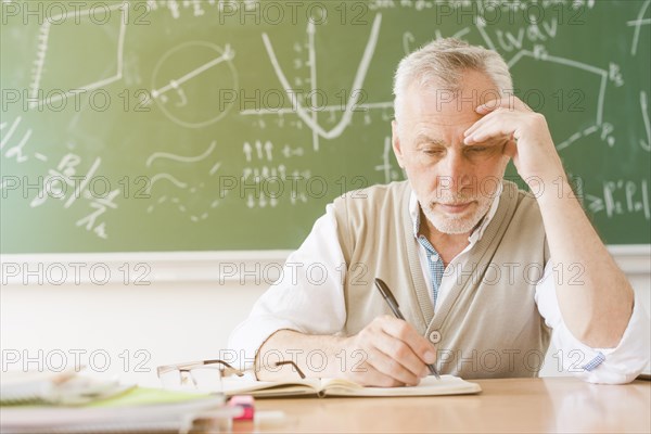 Aged tired teacher writing notebook classroom