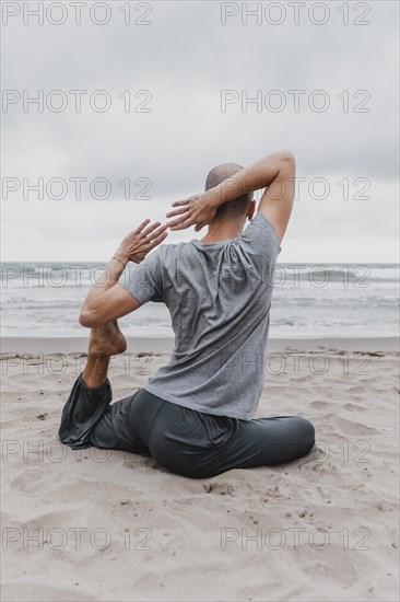 Back view man beach exercising yoga