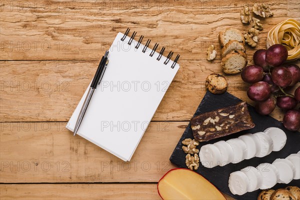 Blank spiral notepad with ballpoint pen near raw ingredients textured background