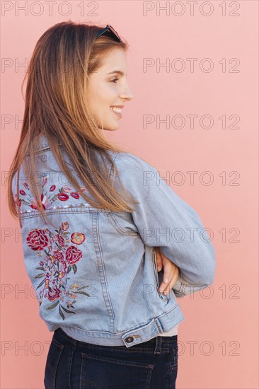 Blonde smiling young woman with her arms crossed against pink background