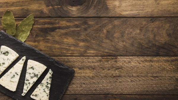 Blue cheese slice arrange black slate with bay leaves old wooden desk