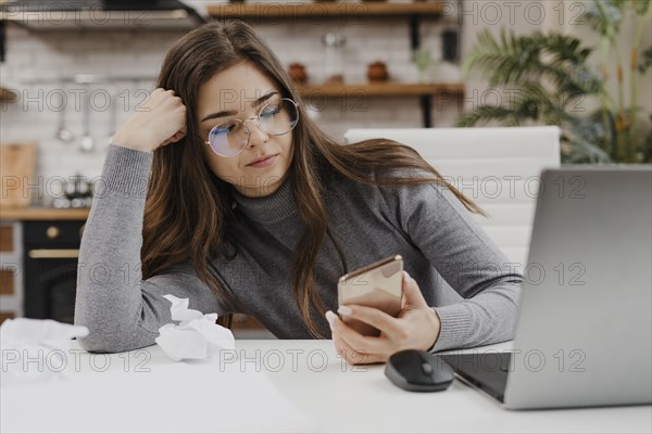 Bored woman checking her phone while working from home