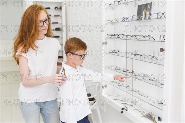 Boy pointing eyeglasses while standing with female optician optica