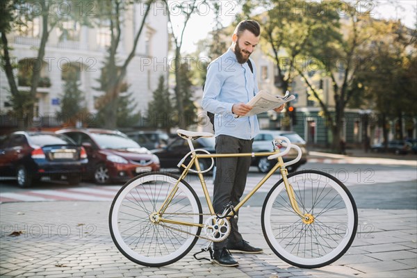 Cheerful man reading newspaper near bike