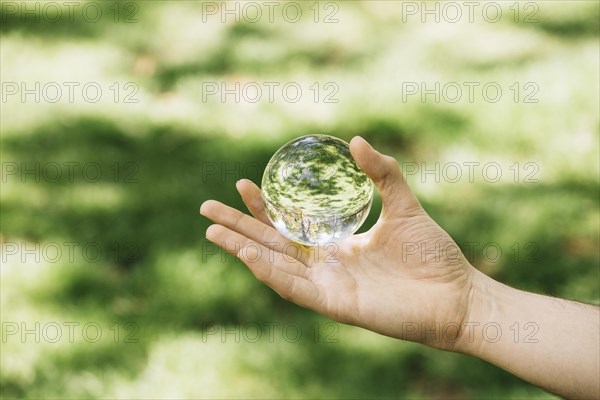 Close up hand holding transparent sphere outdoors