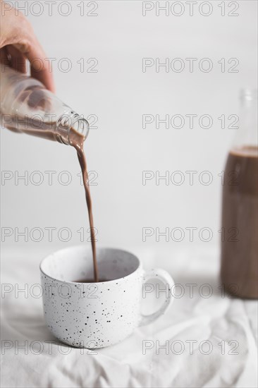 Close up person pouring chocolate milkshake white cup