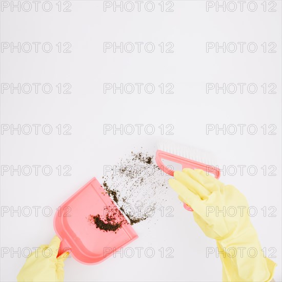 Close up yellow gloved hands sweeping dust into dustpan white background